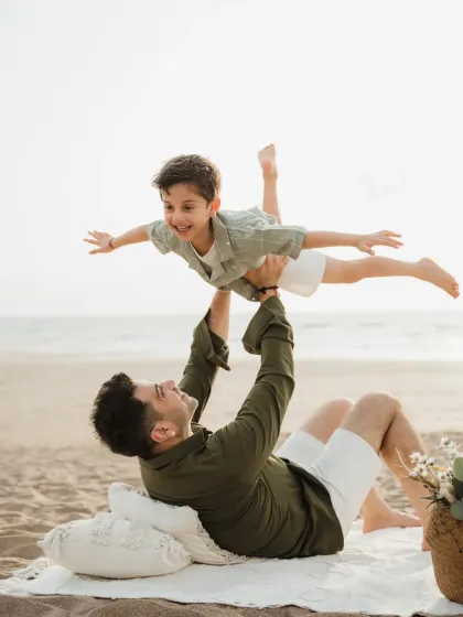 A father playfully lifts his son in the air while lying on the sand. This "airplane" pose is always a hit with kids during beach photoshoots.