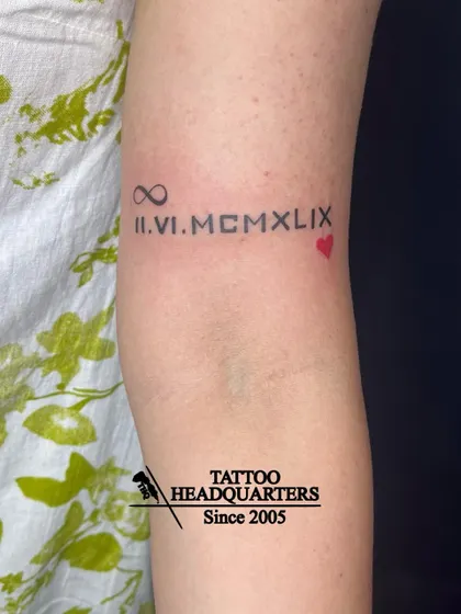 A tattoo of a significant date in Roman numerals, "II.VI.MCMLIX," flanked by an infinity symbol and a heart.