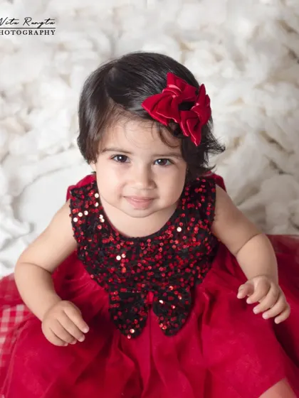 A beautiful close-up portrait of a baby girl, where her expressive eyes and the festive red bow are the stars of the shot.