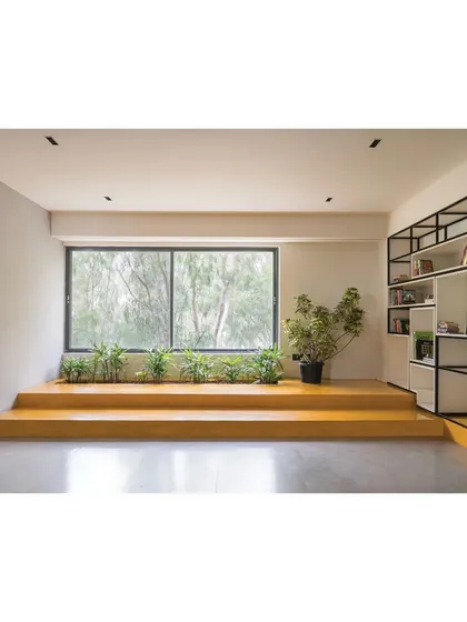 A reading and lounge area in the Meraki Clubhouse, featuring a raised platform with built-in planters. This space offers a quiet retreat with ample natural light and views of the surrounding greenery.