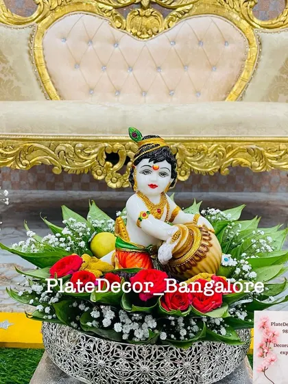 A platter designed for a Krishna Jayanti celebration or pooja, featuring a beautiful idol of little Krishna, surrounded by flowers and leaves.