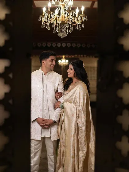 A regal portrait of the couple under a chandelier. The bride's elegant off-white saree and soft makeup create a timeless and sophisticated look for their event.