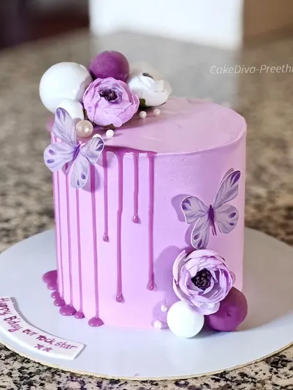 A 6-inch tall drip cake in a lovely pastel shade, created by mixing pink and purple. It's decorated with a ganache drip, delicate wafer paper butterflies, and sugar flowers.