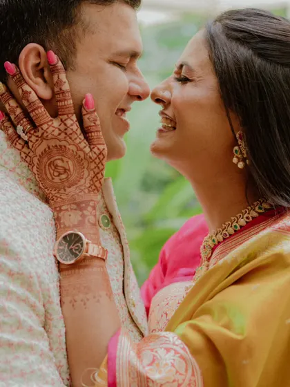 A close-up shot focusing on the bride-to-be's intricate henna design as she lovingly touches her partner's face. This highlights the beautiful details of pre-wedding traditions.
