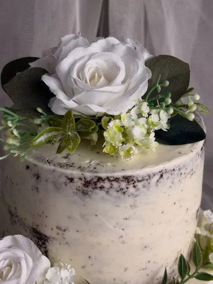 Another angle of the semi-naked cake, focusing on the top tier. The large white silk rose serves as a beautiful focal point, embodying a style that is both rustic and minimalist.