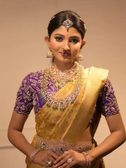A portrait shot showcasing the heavy diamond and emerald jewelry that perfectly complements the golden and purple saree.