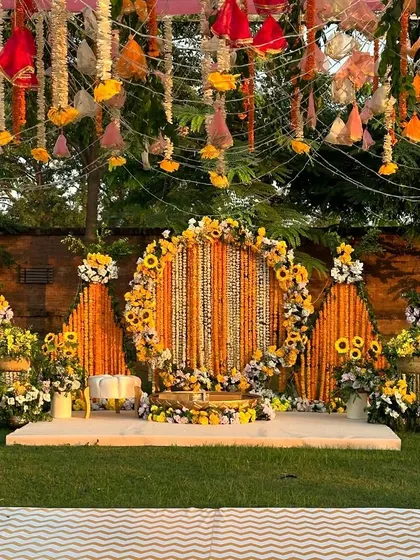 A stunning Haldi stage with a backdrop of marigold strings and a floral arch of sunflowers.
