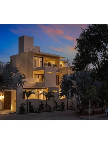 As evening falls, the warm interior light of Casa AUM glows through its many openings, highlighting the home's multi-layered, sculptural form.