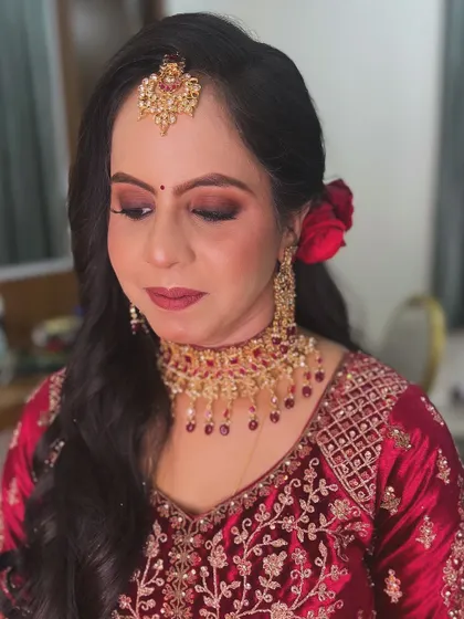 A beautiful reception look in red. The makeup features a warm, smokey eye and a matching red lip, complemented by soft waves and a fresh rose in her hair.