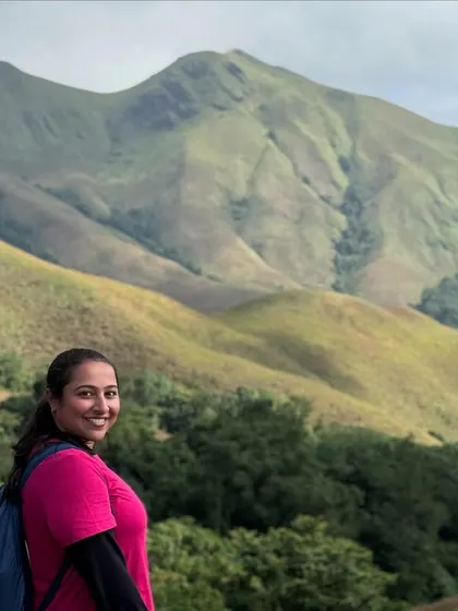 A smiling trekker poses with the stunning Kudremukha mountain range behind her. The views are simply spectacular.