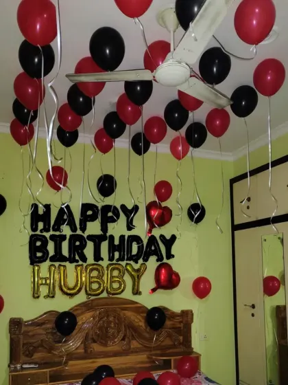 A birthday surprise for 'Hubby' with red and black balloons. The setup includes 'Happy Birthday Hubby' foil letters above the bed.