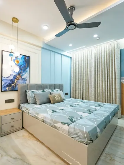 A full view of the bedroom, showcasing the two-tone wardrobe with a mix of blue lacquer and wood finish. The sheer curtains allow for soft, diffused natural light.