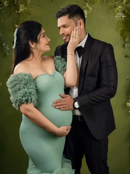 A chic and modern couple's portrait. The mom-to-be wears a stylish mint-green mermaid gown against a complementary green backdrop.
