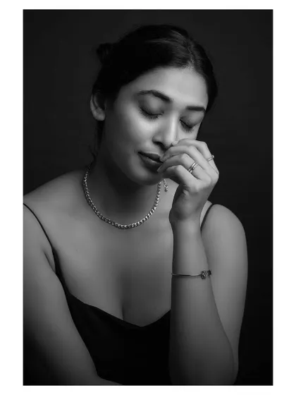 A contemplative black and white portrait. The model's pose and the soft lighting create a sense of quiet introspection and vulnerability.