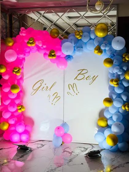 A close-up of the gender reveal backdrop, highlighting the gold text and the vibrant balloon colors.