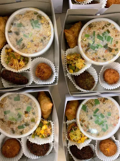 Four snack boxes packed with veg fried rice, mini samosas, mini pizzas, hara bhara kababs, and corn & cheese balls.