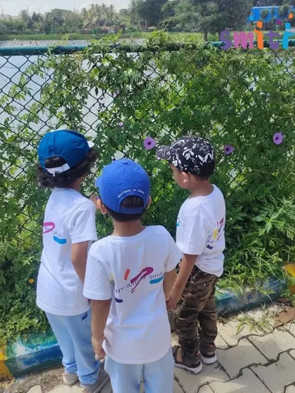 Three boys stop to look at the flowers growing on the fence. Our nature walks encourage children to notice the small details and beauty around them.