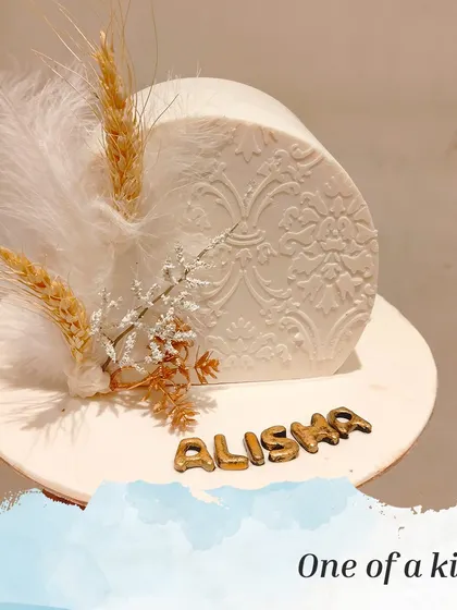 A unique and artistic cake with a textured white finish. The design is accented with dried wheat stalks and feathers, giving it a rustic and bohemian feel.