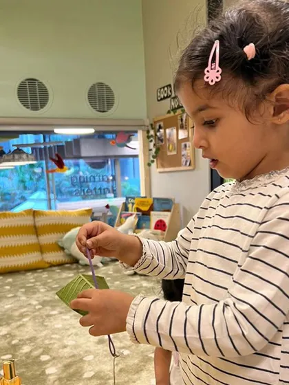 This child is deeply focused on a stringing activity, demonstrating how engaging with natural materials can nurture concentration. This simple act builds patience and refines the pincer grasp.
