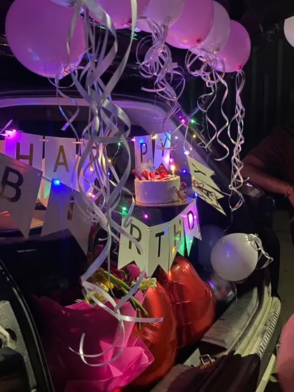 Another angle of a car boot surprise, showing the cake, a bouquet of flowers, and balloons. It's a perfect way to start a birthday celebration.