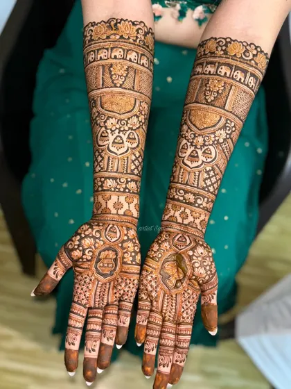 This bridal design is filled with traditional elements, including elephant motifs, hanging bells (jhumkis), and detailed portraits, telling a complete story on the arms.