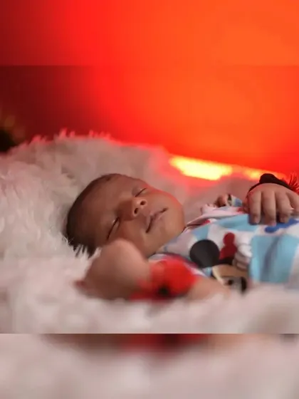 A peaceful close-up of a sleeping newborn. The warm red-orange light in the background adds a beautiful, soft glow to this serene portrait.