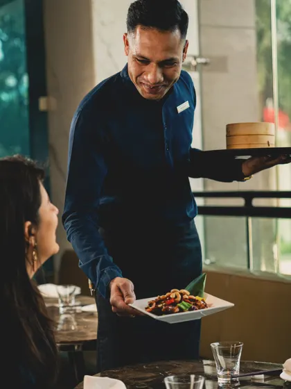This candid shot captures a moment of service at Yauatcha, with a waiter presenting a dish to a guest. It focuses on the interaction and hospitality, telling a story of attentive service and guest satisfaction.