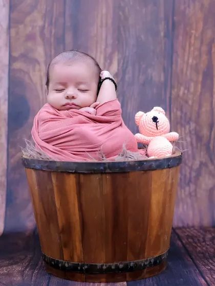 A classic newborn pose, with the baby swaddled and sleeping soundly in a rustic wooden bucket. This highlights their tiny, curled-up form perfectly.