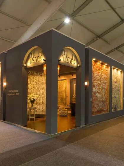 The exterior of the Hands Carpets exhibition booth at NSIC, New Delhi. The design uses arched windows and warm lighting to create an inviting, boutique-like feel, drawing visitors in to explore the collection within.