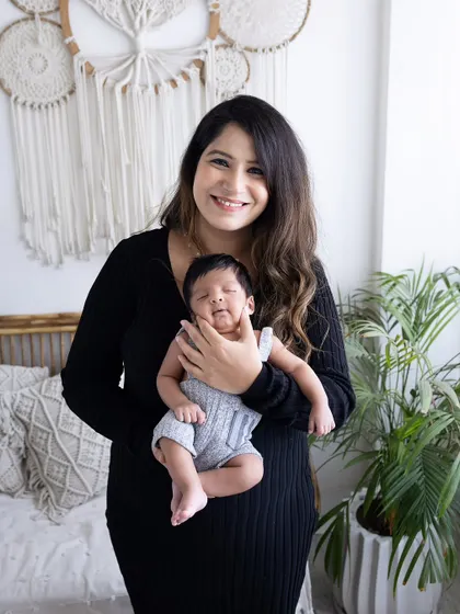 A beautiful portrait of a mother holding her newborn. The baby is dressed in a cute little outfit, and the mother's proud smile says it all.