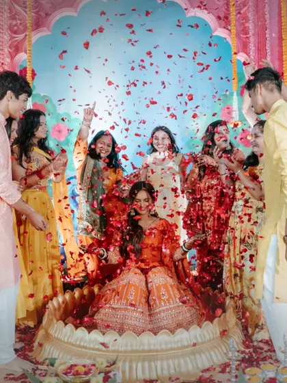 A joyous 'Phoolon ki Haldi' for the bride. She is surrounded by her friends and family as they shower her with red rose petals, creating a beautiful and memorable moment of celebration.