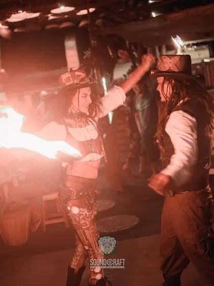 The Steampunk duo performs a fire act together. This image captures a moment of interaction between the two artists during their choreographed routine.