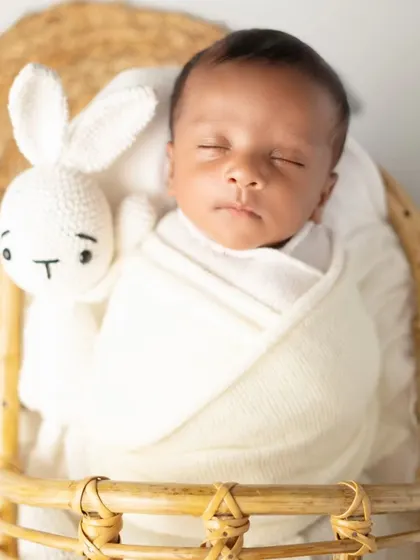 A close-up of the newborn's face, swaddled in white and sleeping next to a knitted bunny. This highlights the peacefulness of a newborn session.