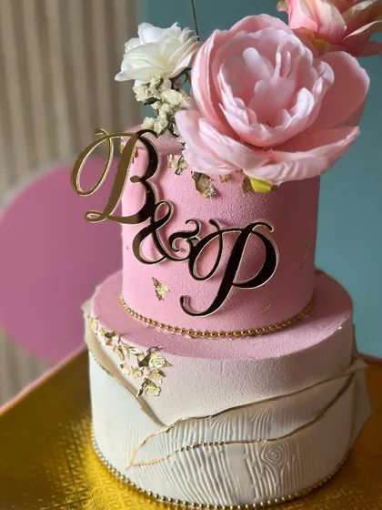 A dreamy and elegant wedding cake in shades of pink and white. This design features a textured bottom tier, a floral-topped upper tier, and a custom initial topper.
