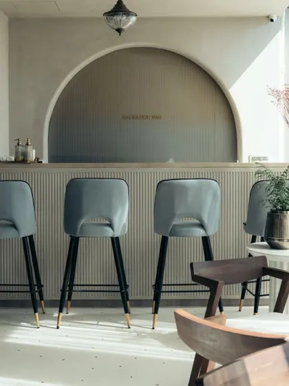 The hydration bar features a fluted counter and elegant high-back stools. I used an arched niche and a neutral, earthy palette to maintain the studio's overall sense of calm and sophistication.