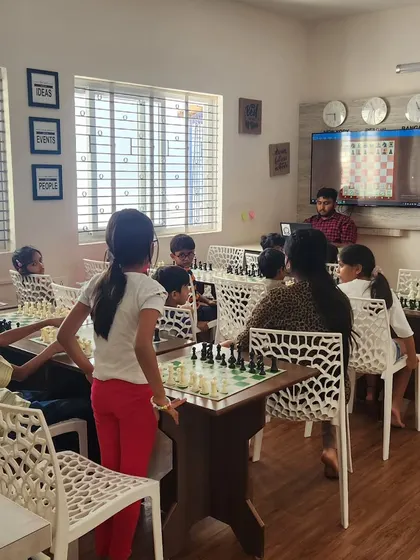 A coach uses a large screen to demonstrate a chess position to the class. We blend traditional board play with modern technology to enhance the learning experience for our students.