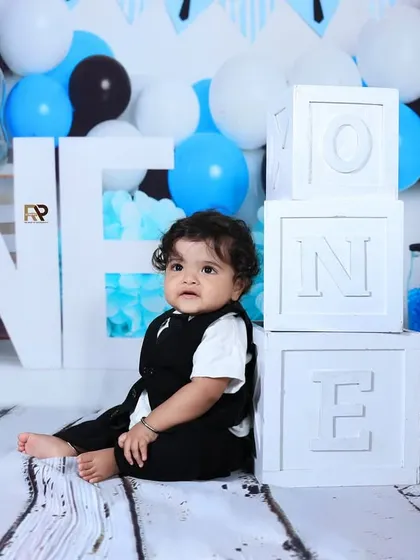 A baby boy sits next to "ONE" blocks in a Boss Baby-themed setup. The cool color palette and props like baby bottles create a unique and humorous first birthday shoot.