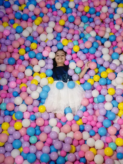 The pure, uninhibited joy of childhood captured as a young girl lies back in a colorful ball pit during her birthday celebration. This playful portrait is full of vibrant colors and happy energy.