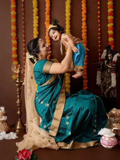 A happy mother lifts her laughing baby girl, both dressed in beautiful traditional attire.
