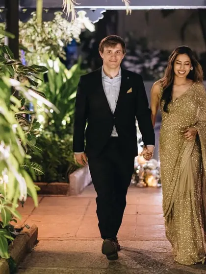 The couple makes their entrance at the cocktail party. Her shimmering gold saree and his sharp suit create a sophisticated and glamorous look.