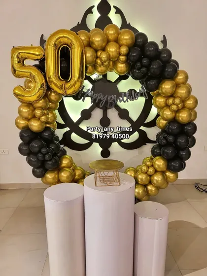A 50th birthday setup featuring a black and gold balloon arch around a unique decorative wheel backdrop.
