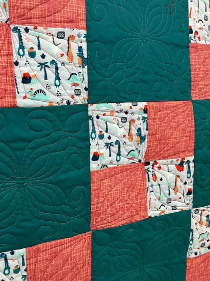 A close-up of the four-patch dinosaur quilt, showing the custom quilting pattern in the solid blocks.