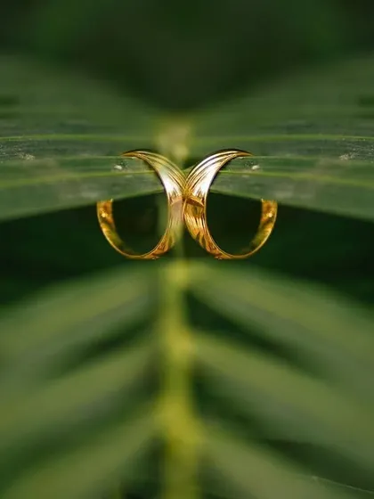 A creative and symmetrical reflection shot of a wedding ring placed on a green leaf. This unique composition connects the symbol of love with the beauty of nature.