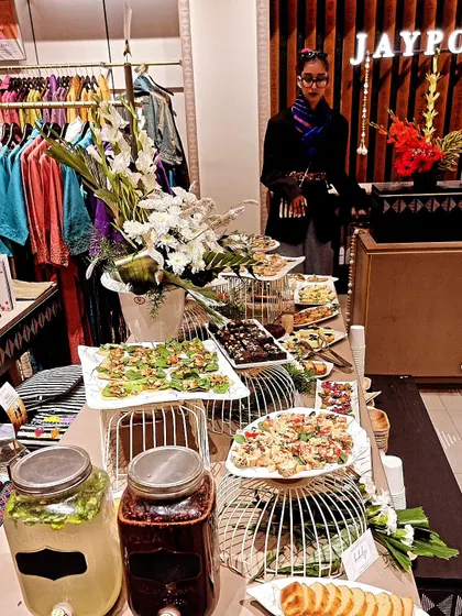 Our Jaypore store grazing table runs beside the clothing displays, with platters of little bites, flowers and two drinks dispensers.