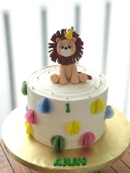 A simple yet regal first birthday cake with a lion topper wearing a party hat.