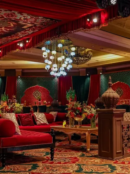 A comfortable lounge area with a red chaise and sofas, set against the backdrop of the patterned ceiling and walls. The space is designed for both grandeur and relaxed conversation.