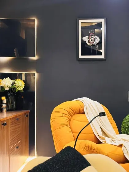 A cozy corner in a multi-purpose studio space, featuring a vibrant orange armchair that adds a bold pop of color against the dark, moody walls.