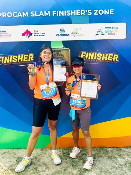 Two of our women runners proudly displaying their finisher medals and certificates at the Procam Slam Finisher's Zone.