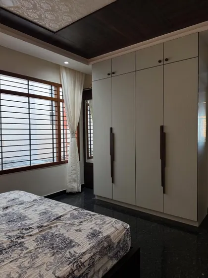 This wardrobe saw your open shelves and said, ‘cute… but let’s elevate’. A sleek, modern white wardrobe with custom wooden handles and a dark wood ceiling detail.