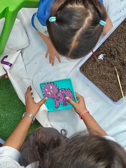 An overhead view of a child and instructor working together on a dinosaur fossil puzzle. This activity teaches patience, precision, and history.